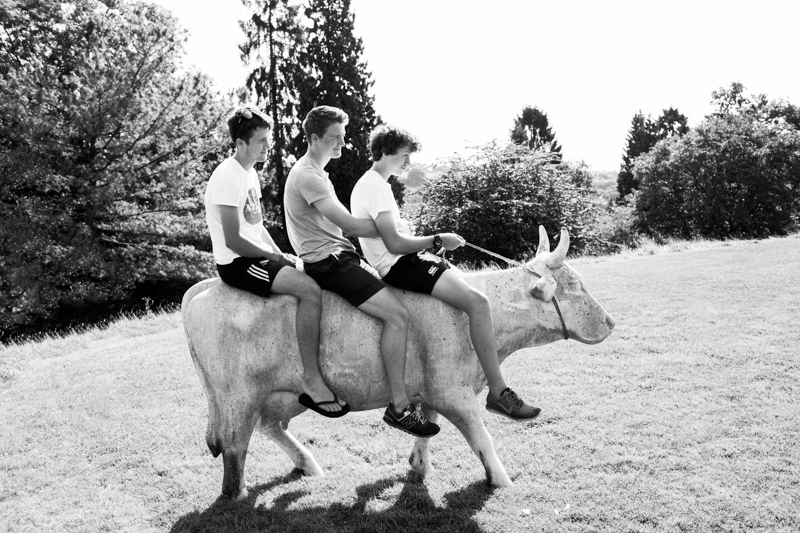 Three teenage boys sitting on a pretend cow.