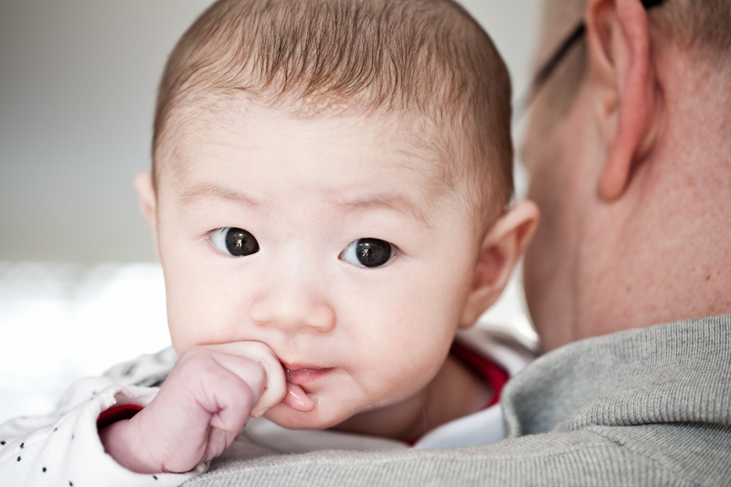 Baby with his and at his mouth looking over man's shoulder. 