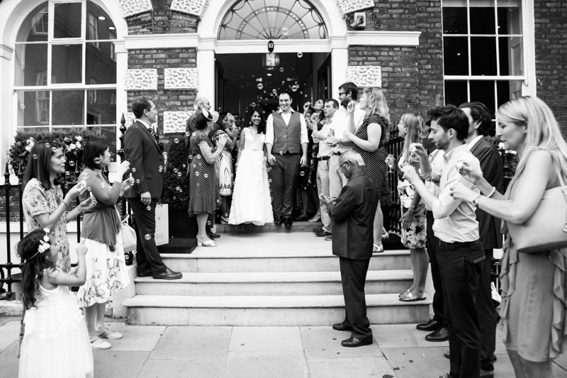 Bride and groom coming down steps with guests blowing bubbles on them. 