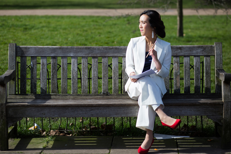 Lady in white suit sitting on bench with paper and pen. 