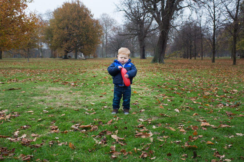 Boy standing in park holding a red balloon.