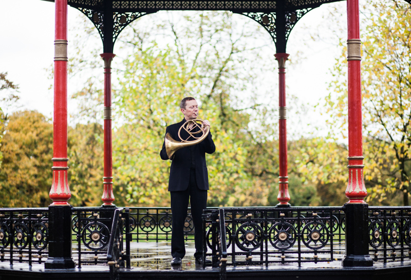 Man playing the French horn in bandstand in park. 