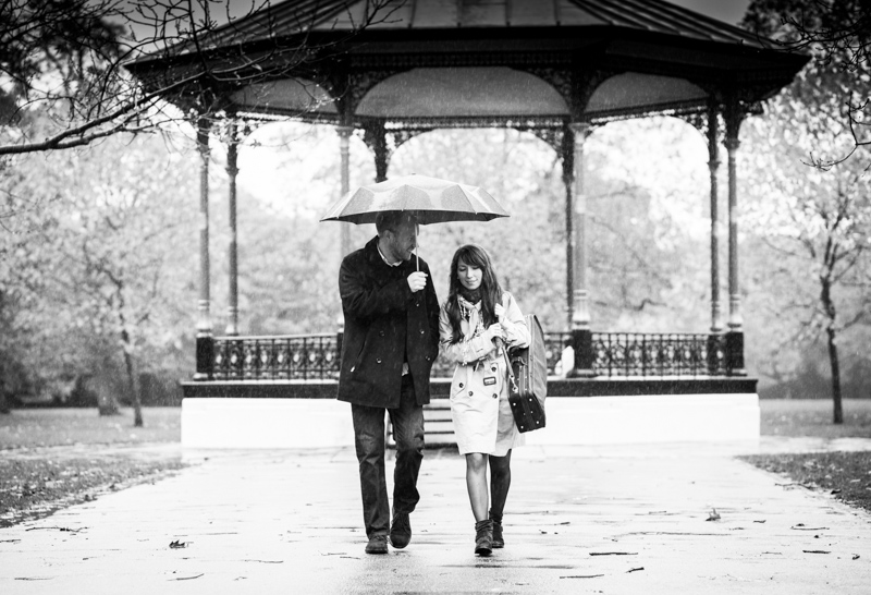 Man and lady with umbrella in front of bandstand. 