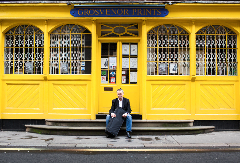 Man sitting on steps in front of yellow shop. 
