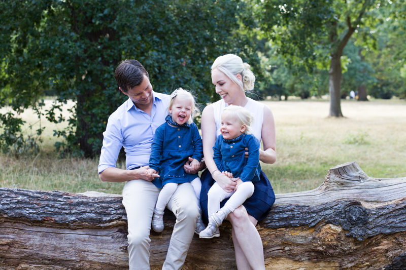 Family of four sitting on a tree trunk laughing. 