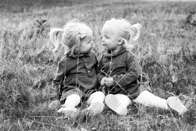Two little girls with ponytails looking at each other sitting on the grass. 