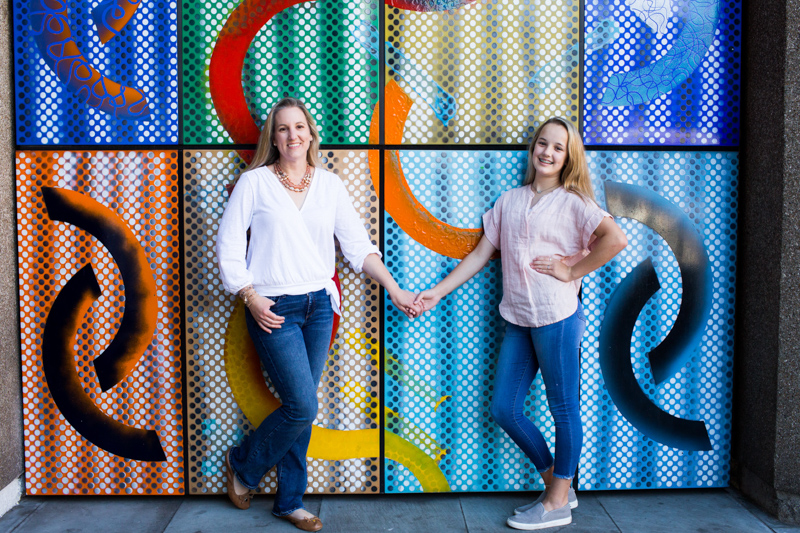 Mum and girl hand in hand in front of bright colourful wall. 