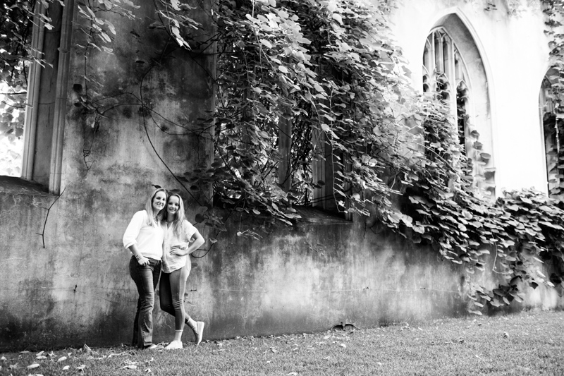 Mother and daughter standing in front of derelict church wall covered in greenery. 
