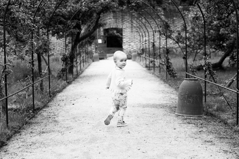 Little girl walking down a path towards brick wall and doorway. 