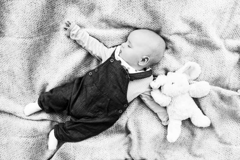Baby in dungarees lying on blanket with toy rabbit. 