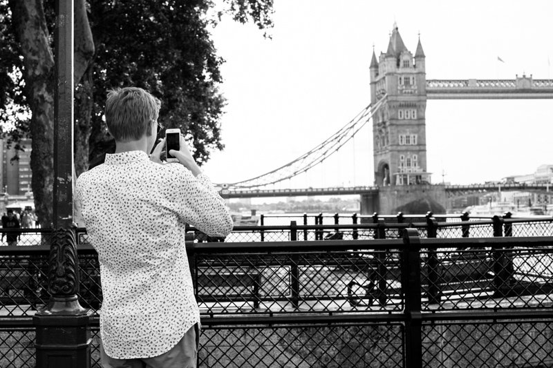 Teenager boy photographing Tower Bridge with iPhone. 