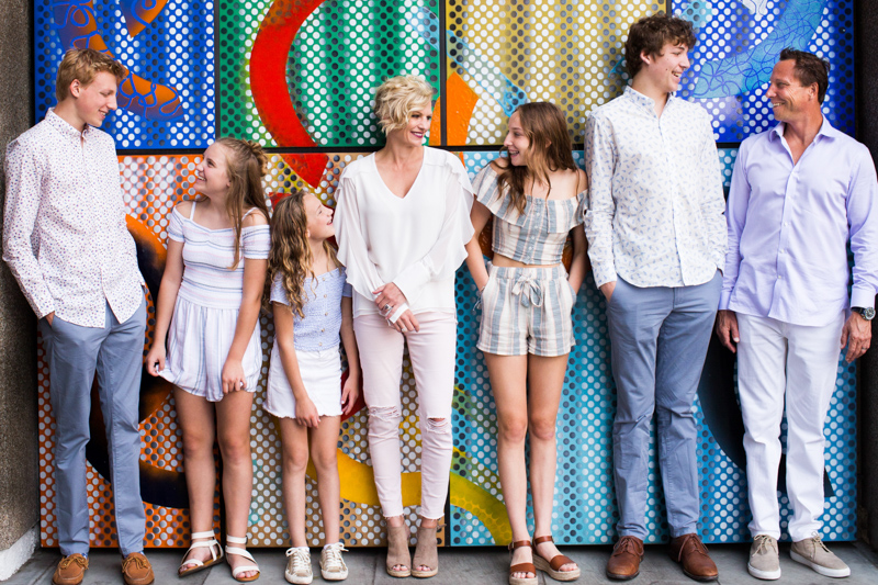 Family of seven in front of colourful wall. 