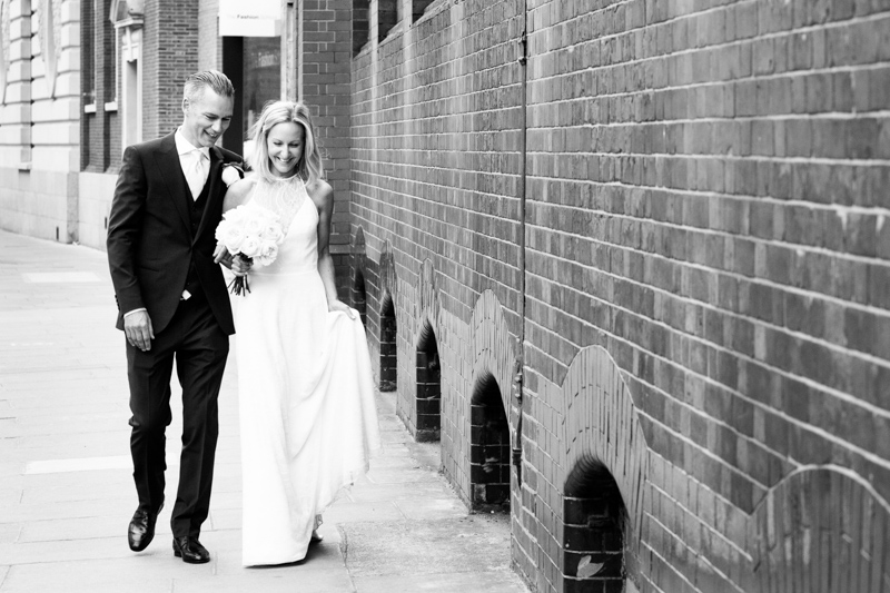 Bride and groom walking past brick wall. 