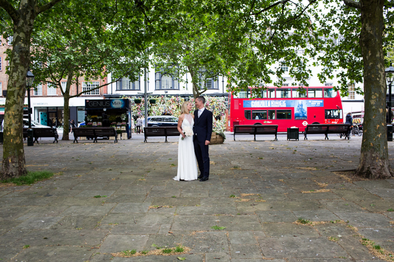 Bride and groom looking at each other with red London bus in the background. 