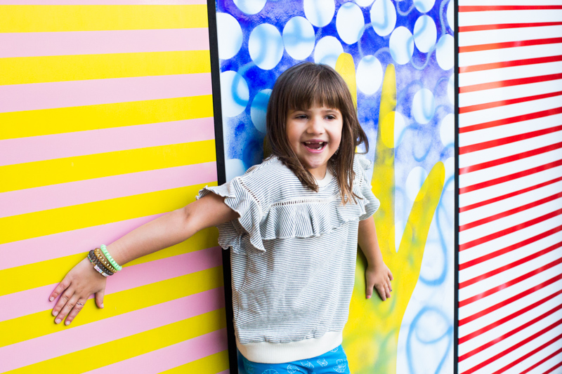 Girl with arms stretched in front of colourful wall.