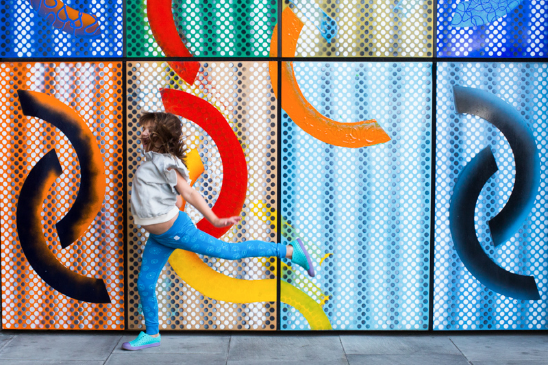 Girl jumping in front of colourful wall. 