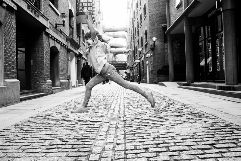 Girl jumping across cobbled street. 