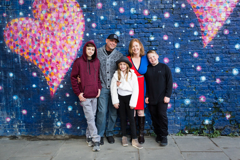 Family of five in front of wall with heart mural on it.