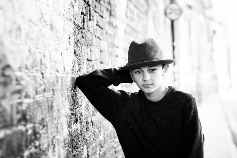 Boy with hat leaning his elbow on brick wall.