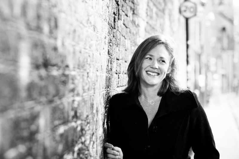 Smiley lady leaning on brick wall.