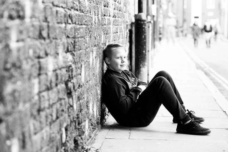 Boy sitting on ground leaning on brick wall.