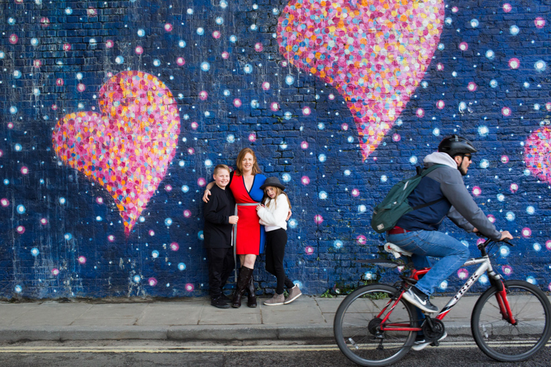 Three people leaning on wall with heart on, with cyclist going past.