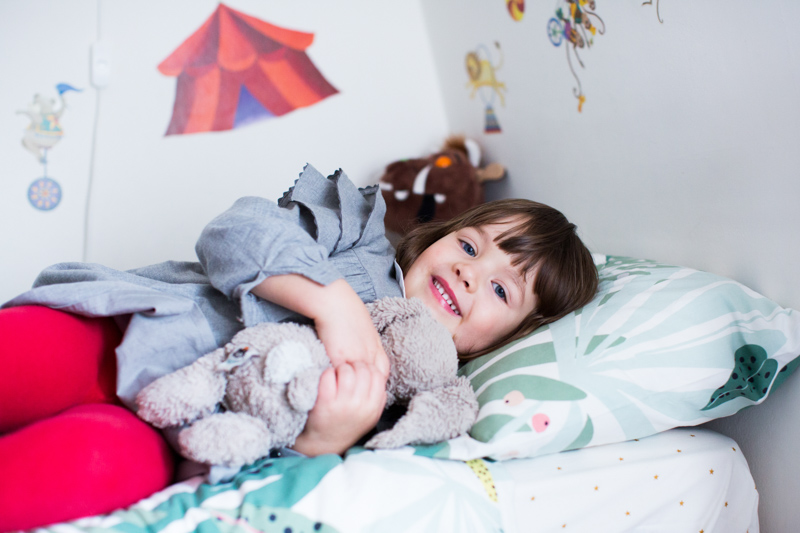 Little girl lying on a bed cuddling her toy.