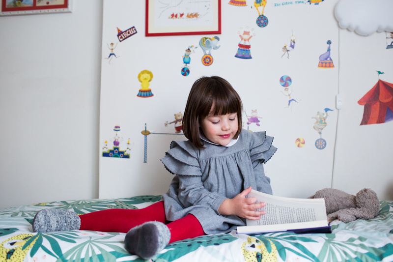 Little girl with red tights reading a book on a bed.