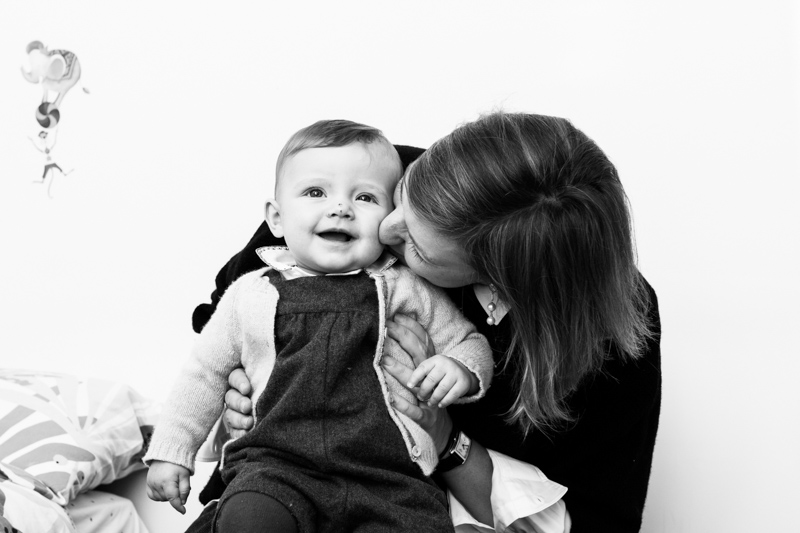 Lady kissing little smiling baby on the cheek.