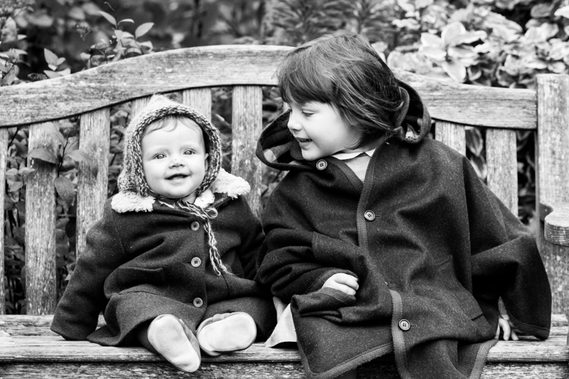 Little girl sitting on bench looking at a baby.
