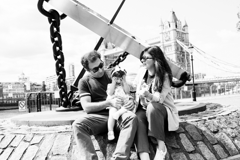 Mum, dad and baby sitting with Tower Bridge in the background. 