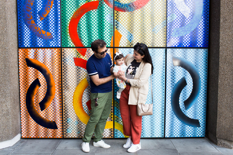 Family of three in front of colourful wall. 