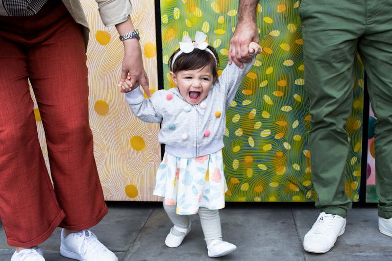 Little girl laughing and holding hands of two grown ups. 