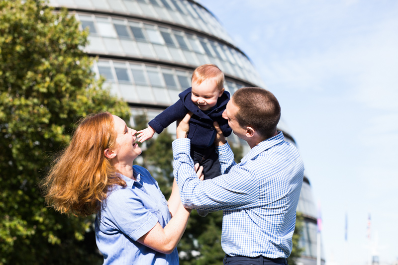 Mum and dad holding their baby up in front of City Hall in London.