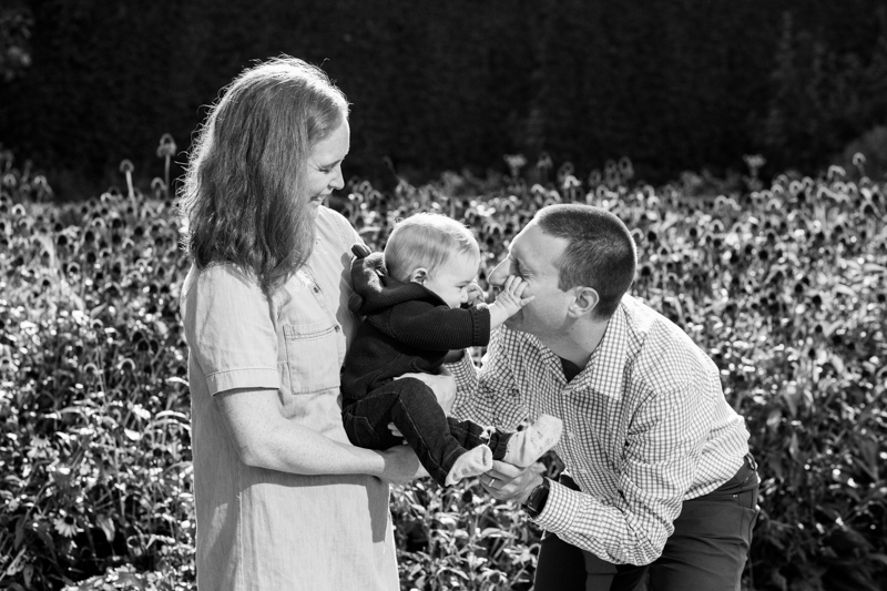 Baby pinching his dad's face in front of flowers.