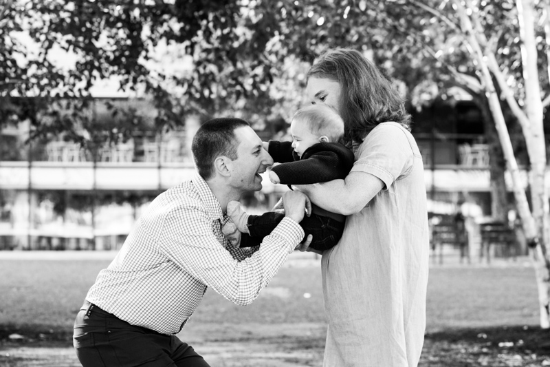 Mum and Dad playing with their baby with trees in the background.