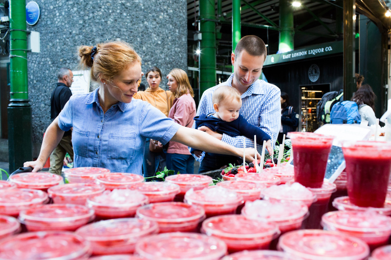 Family of three behind lots of red smoothie drinks.