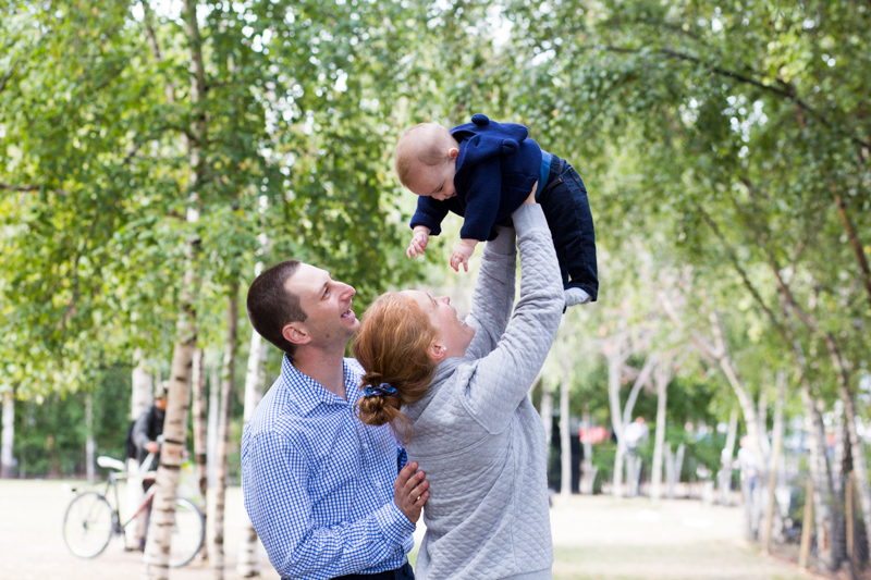 Mum and Dad lifting their baby in the air with trees in the background.