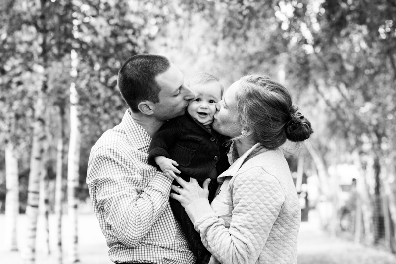 Mum and dad kissing their baby, who is pulling a funny face.