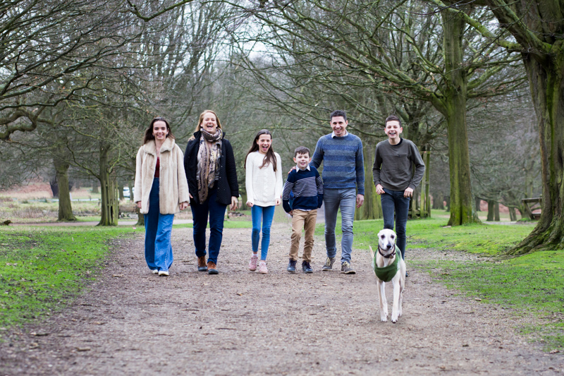 family of six with dog walking along path in the woods