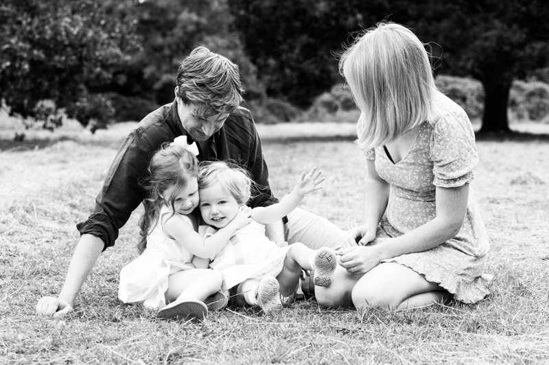 Mum, dad and two daughters sitting on the grass in a park. 