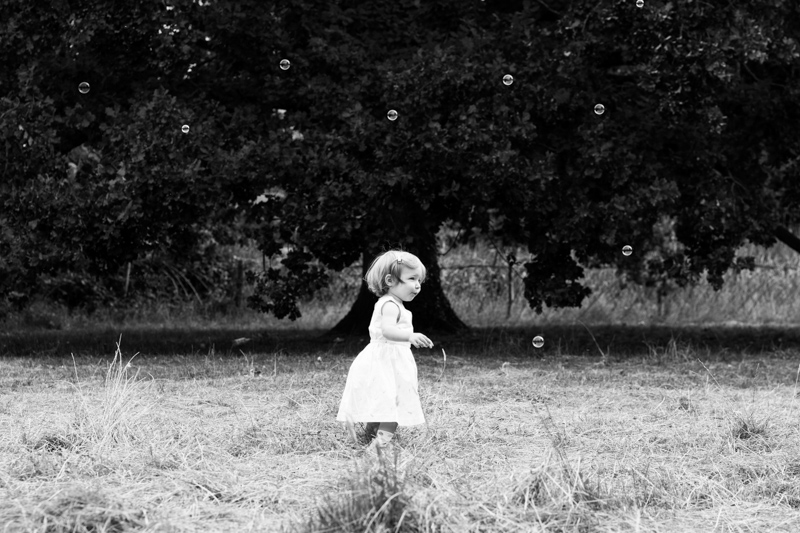 Little girl walking in front of tree surrounded by bubbles. 