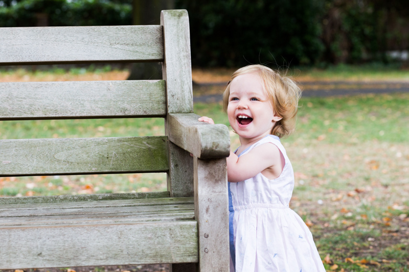 Little girl holding onto a bench laughing. 