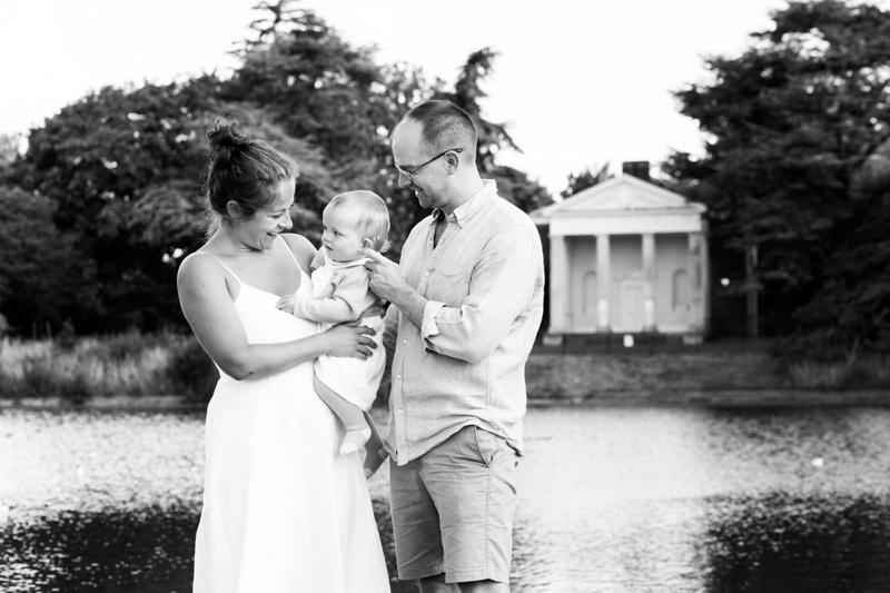 Mummy, daddy and baby girl standing in front of lake. 