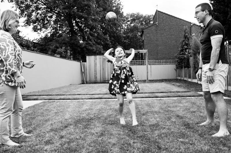 Girl jumping up to catch a ball with man and lady either side of her. 