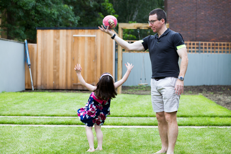 Girl nearly falling over backwards while man holds ball above her. 