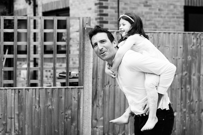 Man pulling a face whilst giving a little girl a piggy back. 