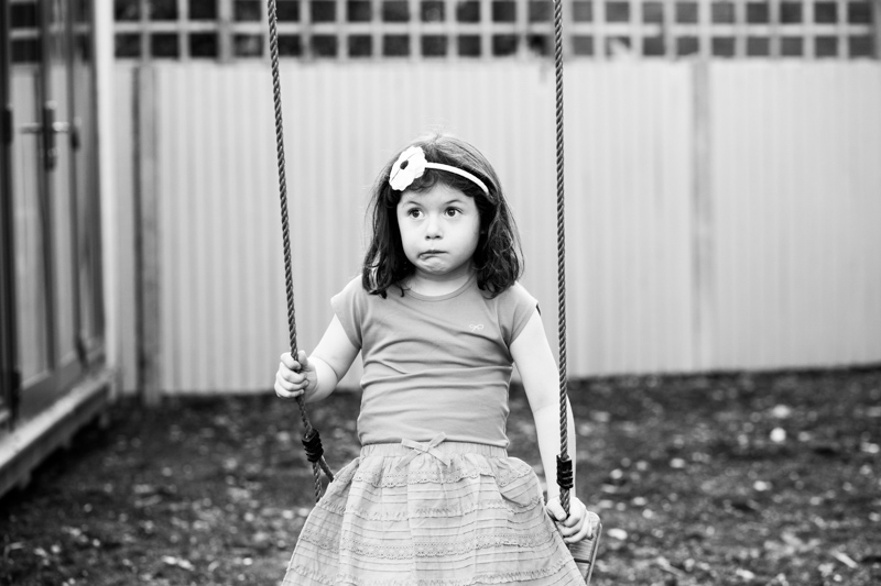 Little girl pulling a funny face whilst sitting on a swing. 