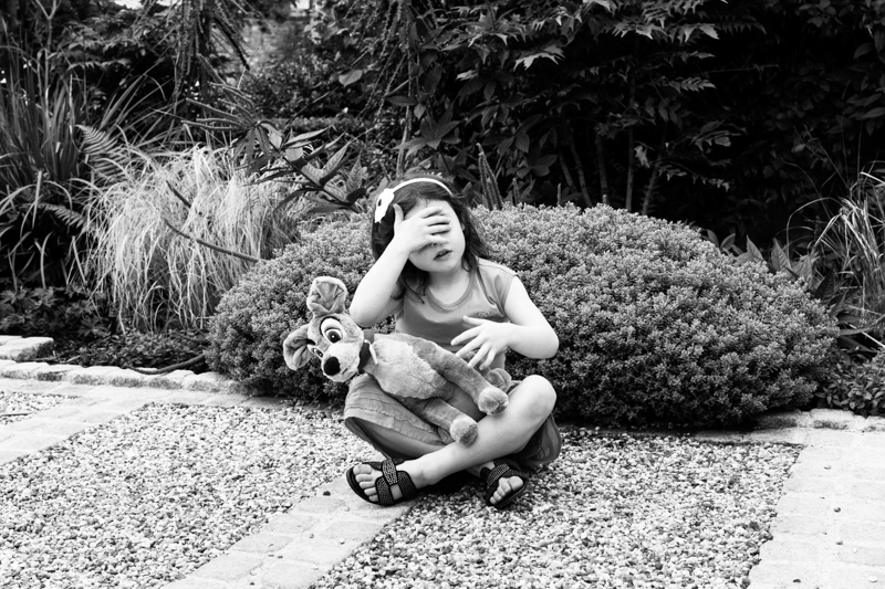 Girl covering her eyes and holding toy. 