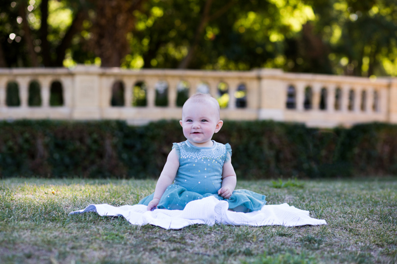 Baby girl sitting on a white blanket on the grass.